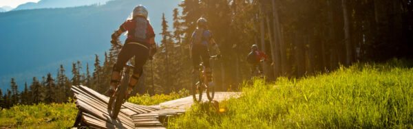 Two mountain bikers riding a dirt trail through dense alpine forest at Mount Washington.